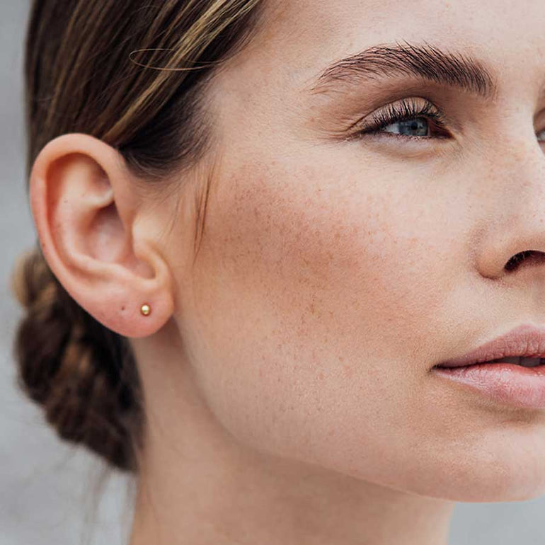 Minimalistische elegante Frau trägt Kugel Ohrstecker designt in Gold