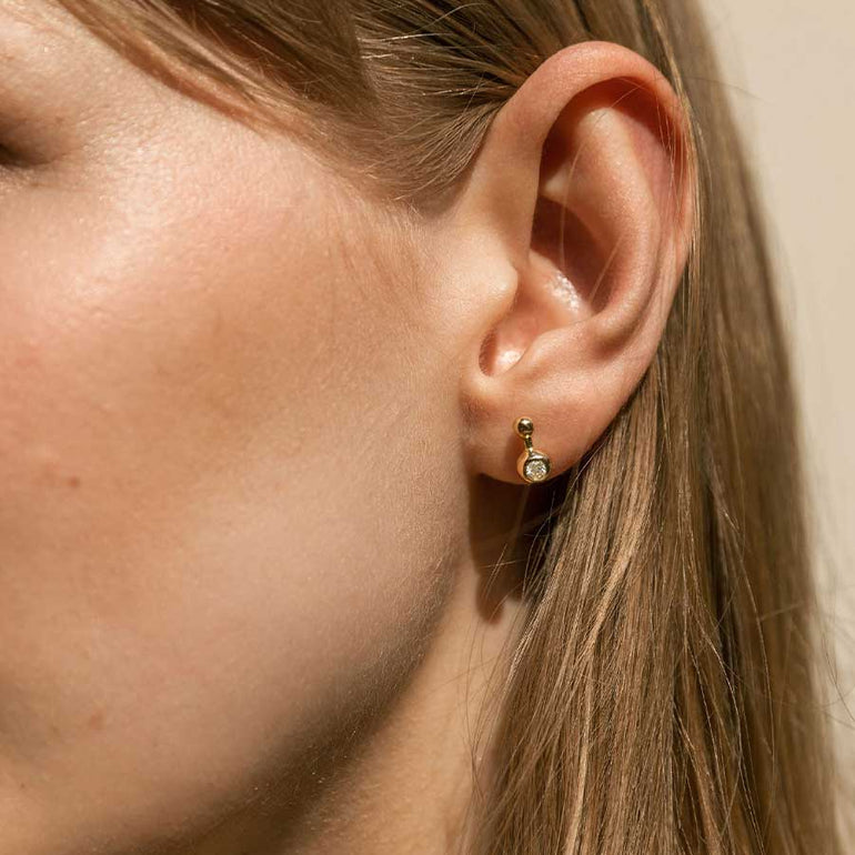 Besonderer Kugelohrring aus recyceltem Gold und mit Labordiamant besetzt von Maren Jewellery am Ohr eines Models im Sonnenschein