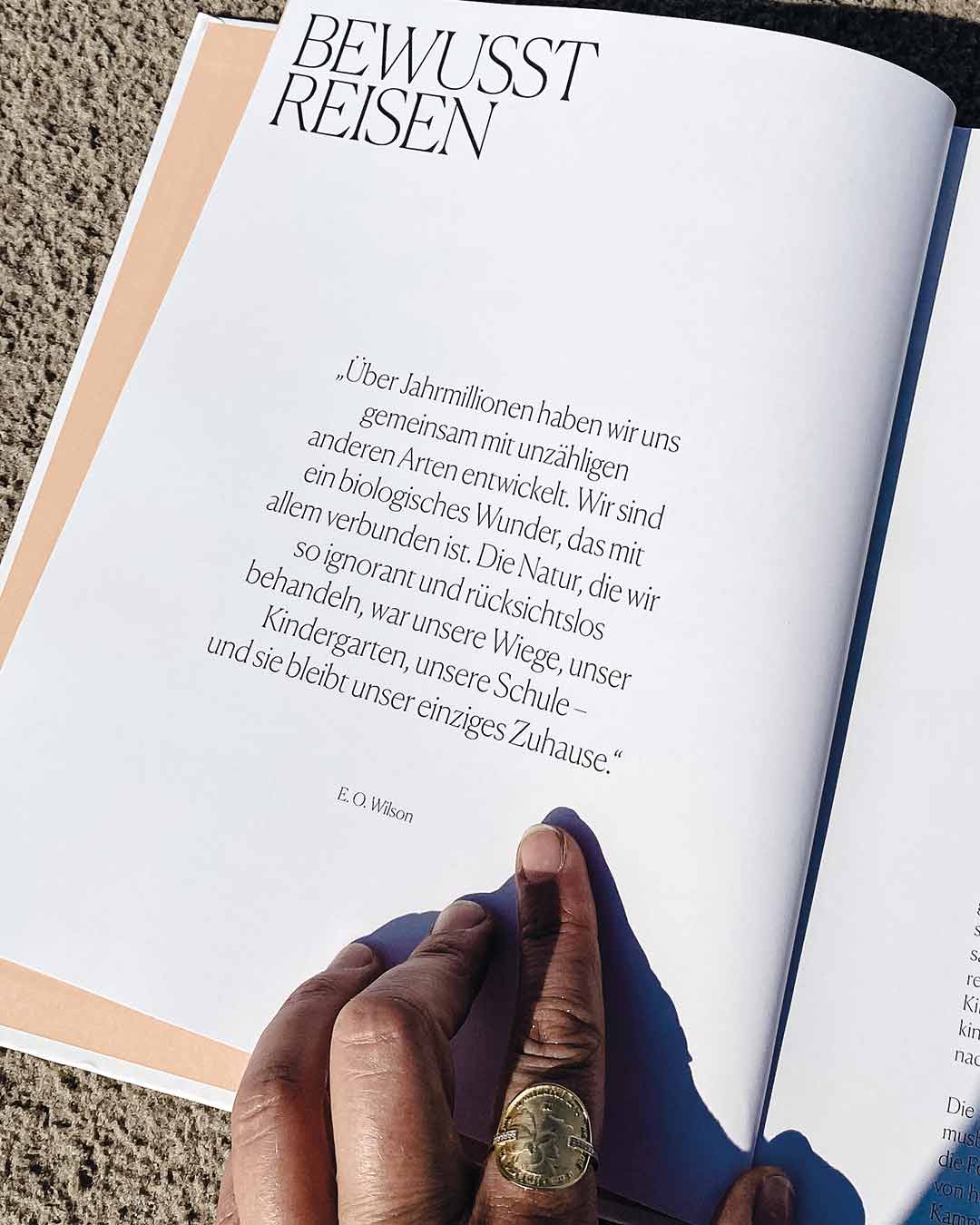 Eine Hand mit dem achtsamen Wild Flowers Münzring von Maren Jewellery hält ein Buch über bewusstes Reisen auf