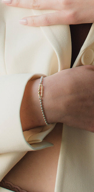 Detailaufnahme des Handgelenks einer Frau in hellem Blazer, die ein nachhaltiges silbernes Kugelarmband mit Gelbgold Verschluss trägt