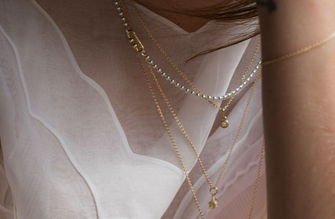 Nahaufnahme on unterschiedlichen nachhaltigen Ketten von Maren Jewellery in unterschiedlichen Farben am Hals eines Models in weißem Kleid