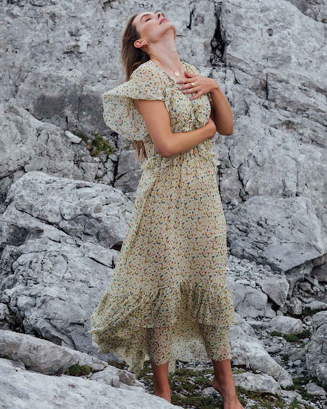 Junges Model in zartem Blumenkleid vor felisgem Hintergrund lässt sich vom Wind anwehen und zeigt nachhaltigen Schmuck von Maren Jewellery