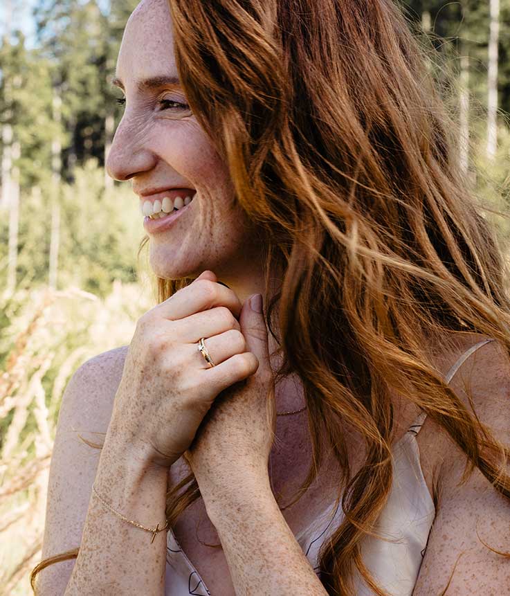 Potrait einer strahlenden jungen Frau in der Natur die Schmuck aus recyceltem Gold von Maren Jewellery trägt