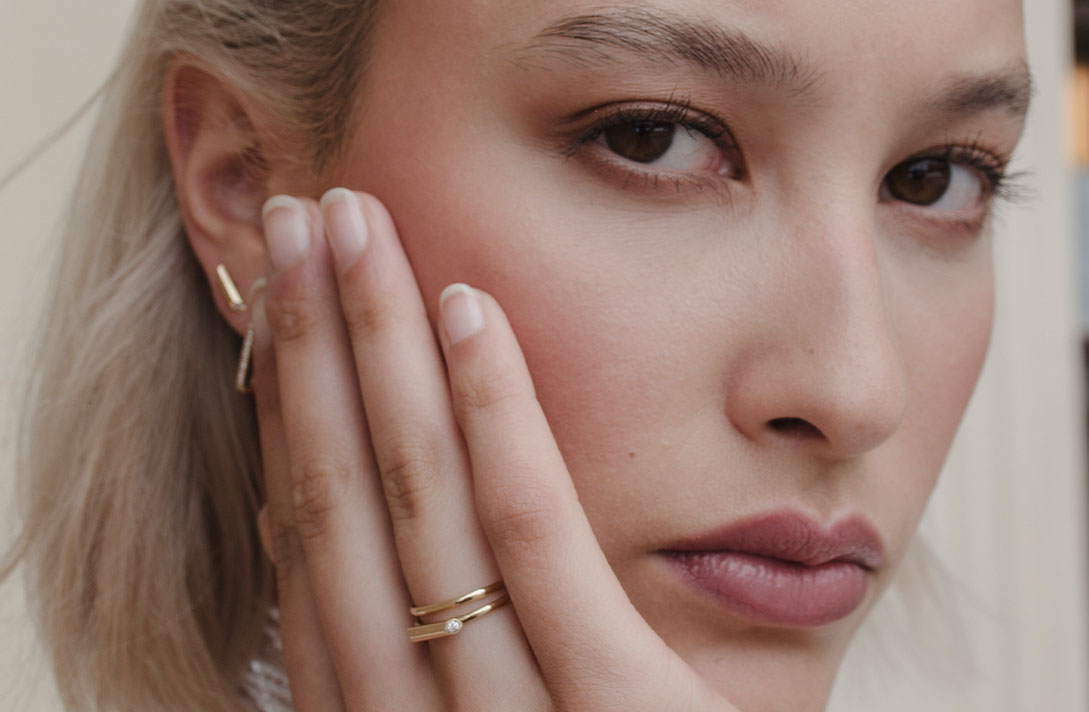 Porträtaufnahme eines Modells, das sein Gesicht in die Hand stützt an dem es seinen Verlobungs- und Ehering con Maren Jewellery kombiniert trägt