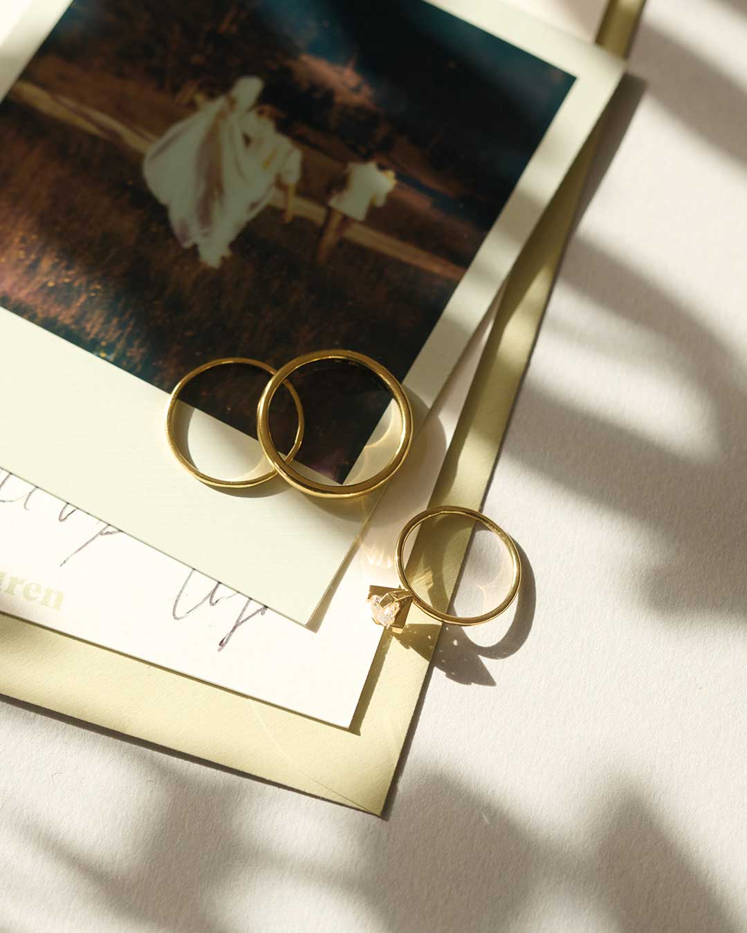 Nachhaltige Ehe- und Verlobungsringe von Maren Jewellery aus recyceltem Gold im Halbschatten auf Polaroid Fotos einer Hochzeit