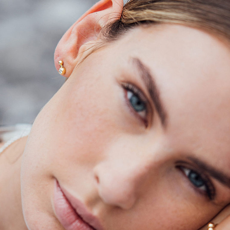 Extravagnter Kugelohrstecker aus recyceltem Gold mit Labordiamant von Maren Jewellery am Ohr eines Models, das verträumt in die Kamera schaut