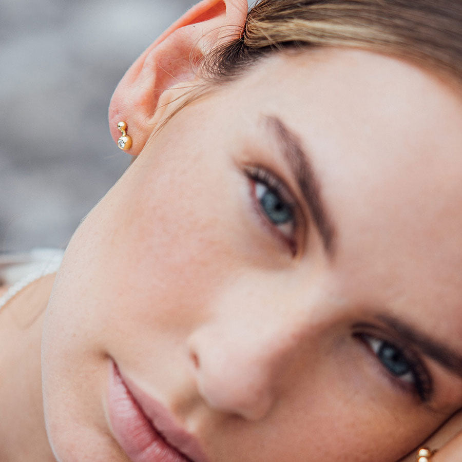 Extravagnter Kugelohrstecker aus recyceltem Gold mit Labordiamant von Maren Jewellery am Ohr eines Models, das verträumt in die Kamera schaut