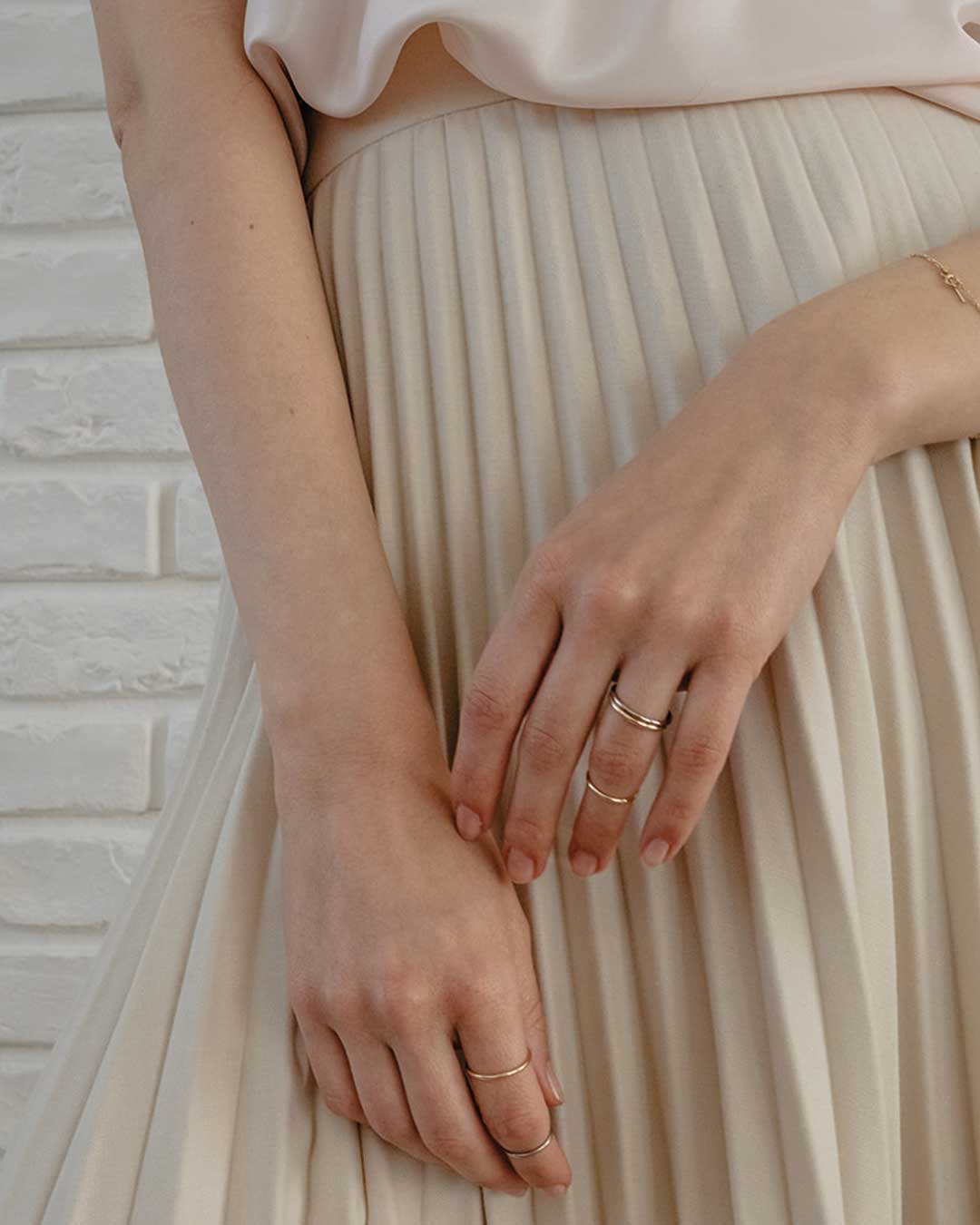 Model zeigt feinen minimalistischen Schmuck aus recyceltem Gold von Maren Jewellery vor ihrem dezenten Faltenrock