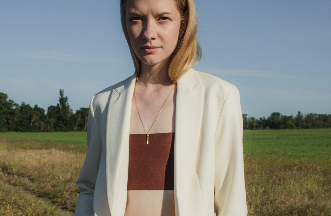Junges Model in der Natur schaut ins Gegenlicht und präsentiert einen nachhaltigen Goldanhänger von Maren Jewellery passend zur Hochzeit.