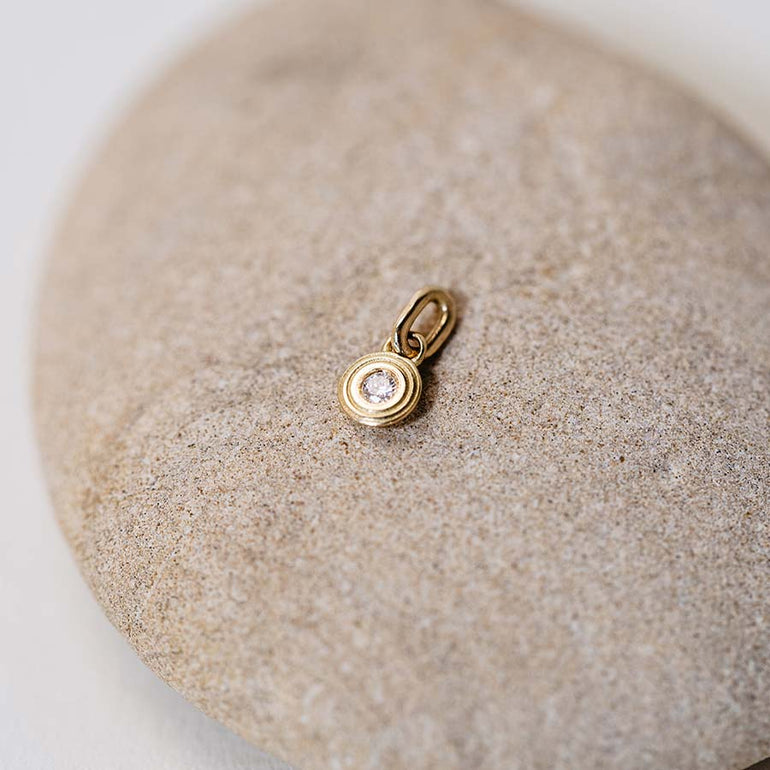 Zarter Mini Anhänger aus recyceltem Gold und mit Labordiamant besetzt von Maren Jewellery liegt auf einem großen Kieselstein