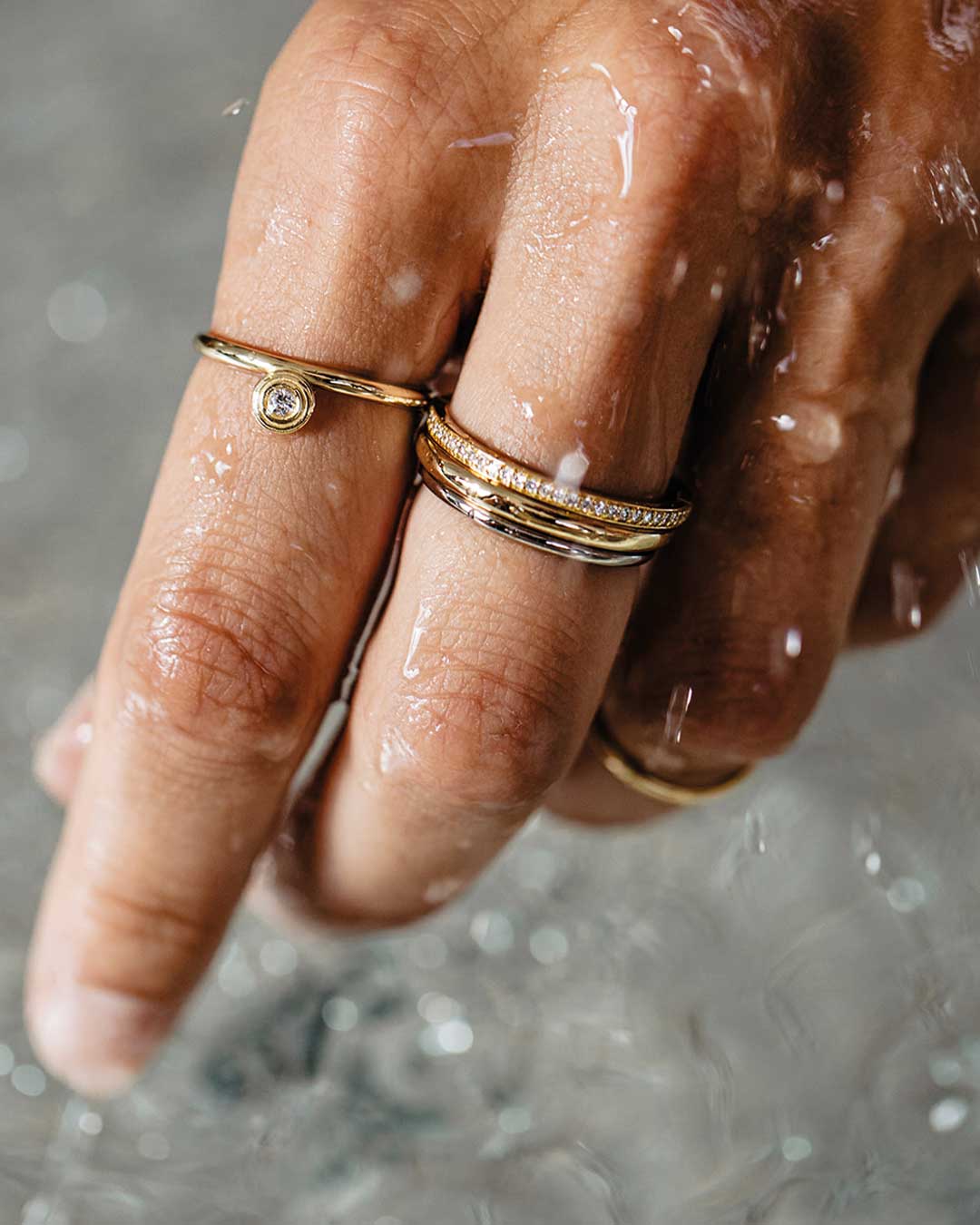 Nahaufnahme einer Frauenhand die durchs Wasser fährt und nachhaltige Ringe von Maren Jewellery aus recyceltem Gold und Labor Diamanten trägt