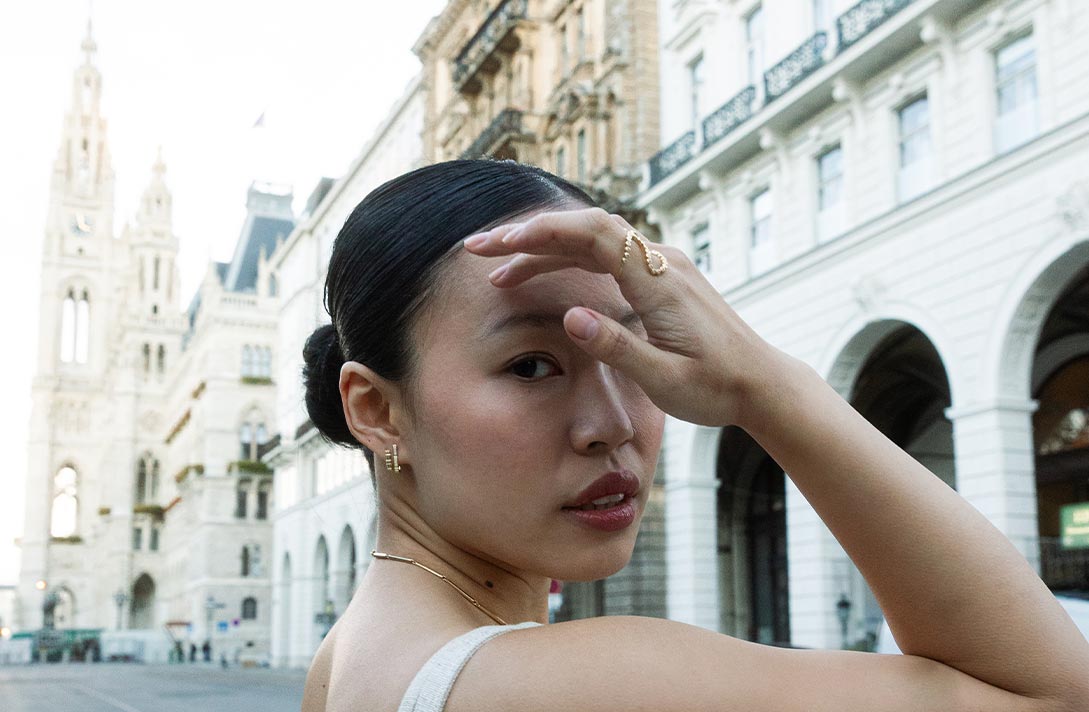 Model vor klassizistischer Innenstad Fassade blickt über ihre Schulter und präsentiert nachhaltigen Schmuck von  Maren Jewellery aus recyceltem Gold und Labordiamanten