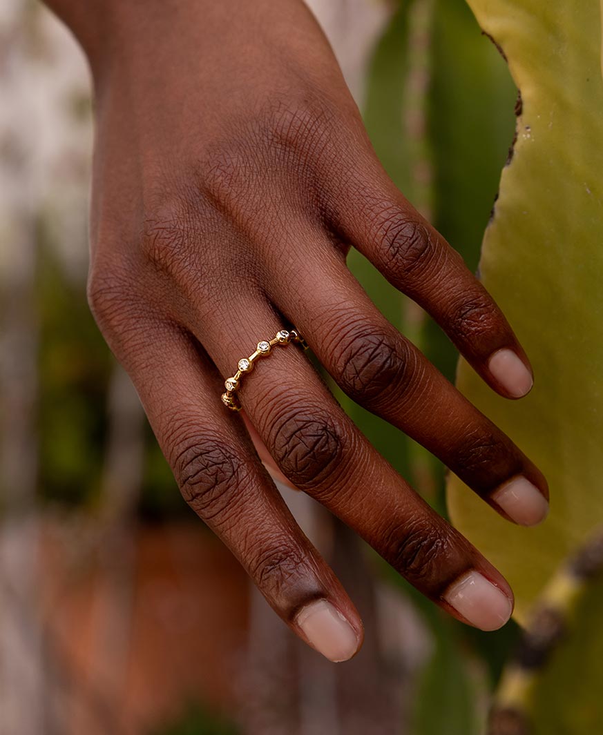 Infinity Verlobungsring von Maren Jewellery aus recyceltem Gold und mit Labordiamanten besetzt an der Hand eines Models vor grünen Pflanzen