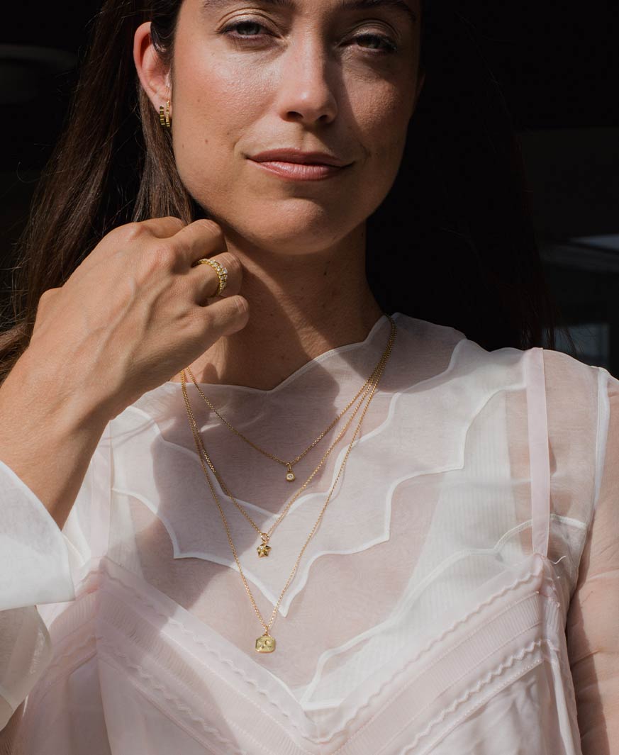 Potraitaufnahme eines Models im weißen Kleid, das drei unterschiedlich lange Ketten von Maren Jewellery aus recyceltem Gold um ihren Hals trägt