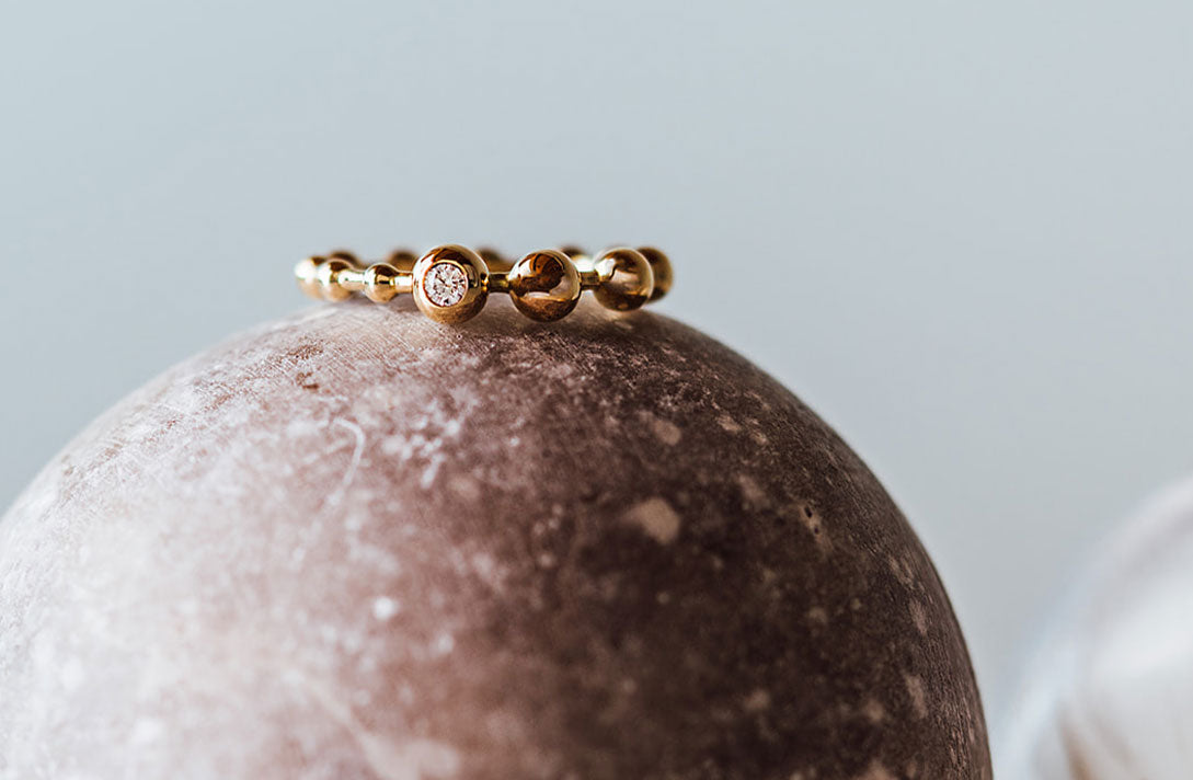 Nahaufnahme des Kugelrings von Maren Jewellery aus recyceltem Gold und mit Labordiamant besetzt auf einem Kugelstein