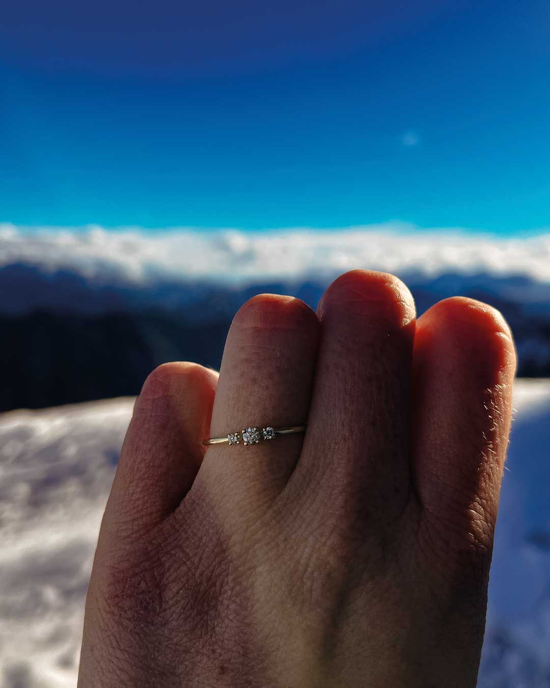 Photo of a satisfied customer’s hand wearing her sustainable engagement ring from Maren Jewellery on a snow-covered mountain peak with mountains in the background