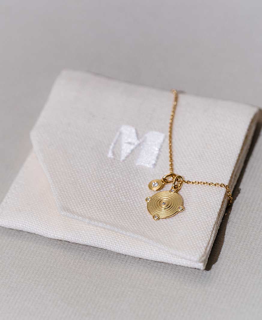 Nachhaltiges Leinen Etui für Schmuck, um das eine Goldkette mit Anhängern aus recyceltem Gold und Labordiamanten geschlungen ist.