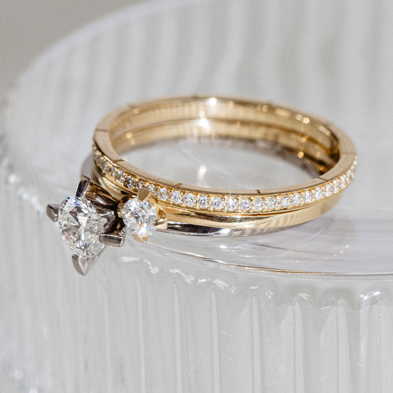Memoire Ehe- und Verlobungsringe aus recyceltem Gold und it Labordiamanten von Maren Jewellery liegen gestackt auf einem Glas
