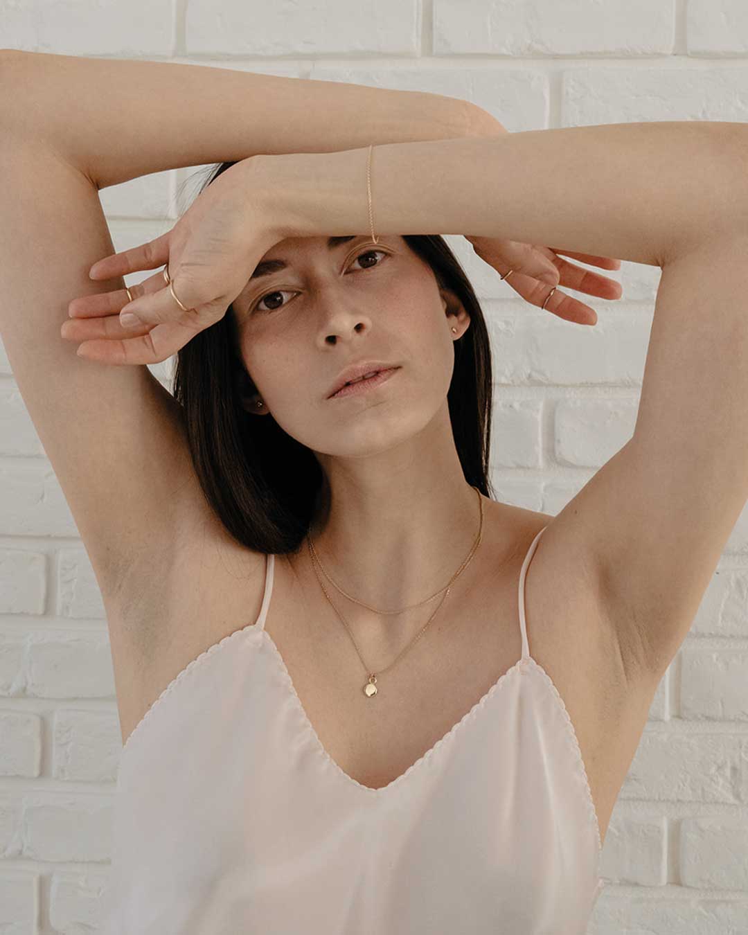 zartes Model schaut in die Kamera, hält ihre Arme vor ihrer Stirn und zeigt den nachhaltigen Schmuck von Maren Jewellery