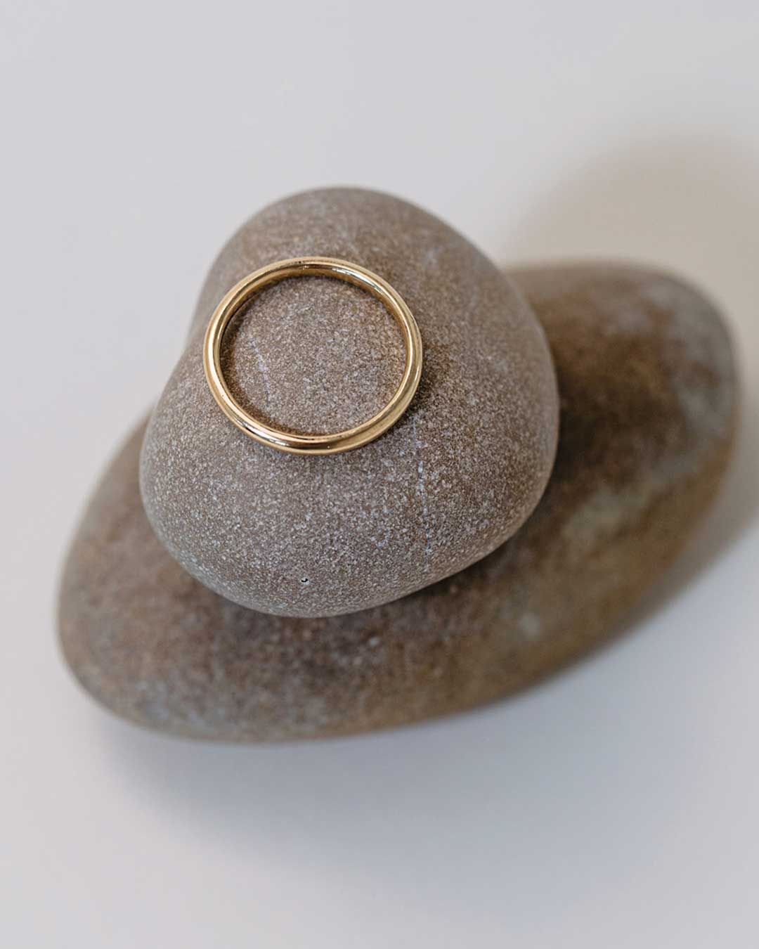 Detailaufnahme von oben zeigt einen minimalistischen Ehering aus recyceltem Gold von Maren Jewellery, der auf einem Kieselsteinturm liegt