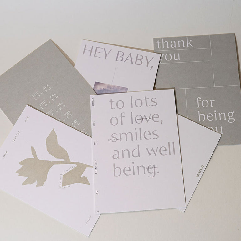 Postkarten übeineander liegend auf tisch minimalistisch mit viel Text in weiß grau und beige Tönen