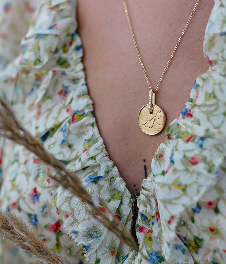 Detailaufnahme, die einen Münzanhänger aus recyceltem Gold an der Kette eines Models zeigt