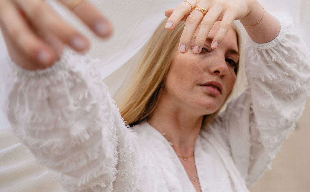 Model in weißem Kleid trägt nachhaltige Goldringe von Maren Jewellery und spielt verträumt mit ihrem Schleier