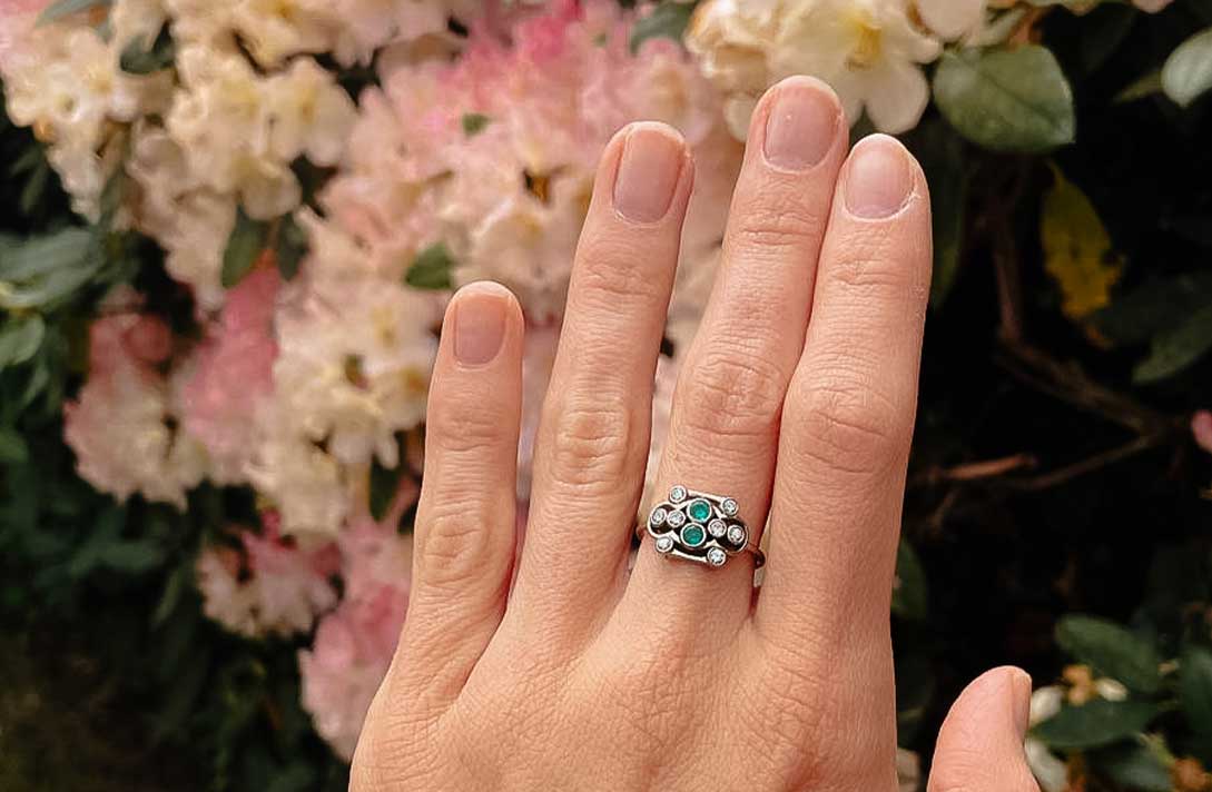 Hand mit Ring mit grünen Steinen und weißen Diamanten
