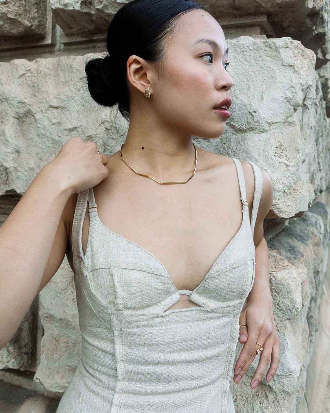 Model lehnt sich gegen eine massive Steinfassade und präsentiert den eleganten und zarten Schmuck von Maren Jewellery aus recyceltem Gold und Labordiamanten