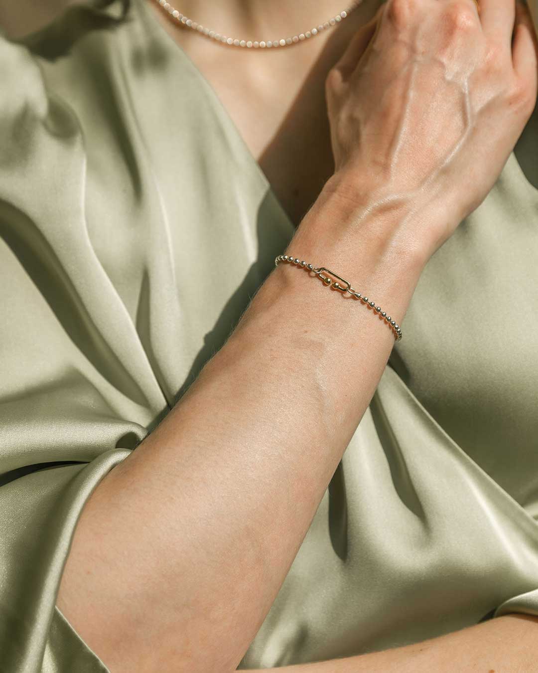 Silverkette von Maren Jewellery mit 18ct Gelbgoldverschluss am Handgelenk eines Models vor hellgrünem Kleid in warmen Sonnenlicht