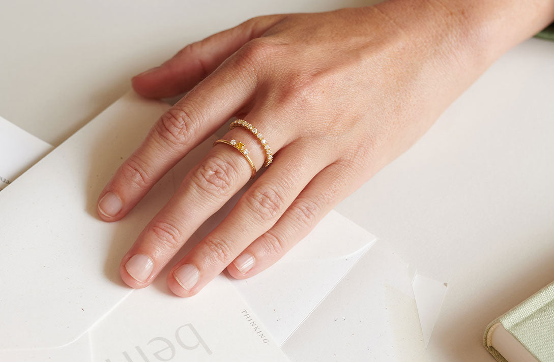 Slow Luxury Verlobungsringe von Maren Jewellery aus recyceltem Gold und Labordiamanten an der Hand eines Models über weißen Papieren als Hintergrund