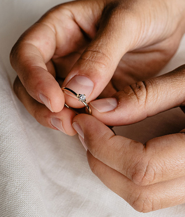 Hände halten einen zarten Solitär Verlobungsring aus recyceltem Gold mit Labor Diamant