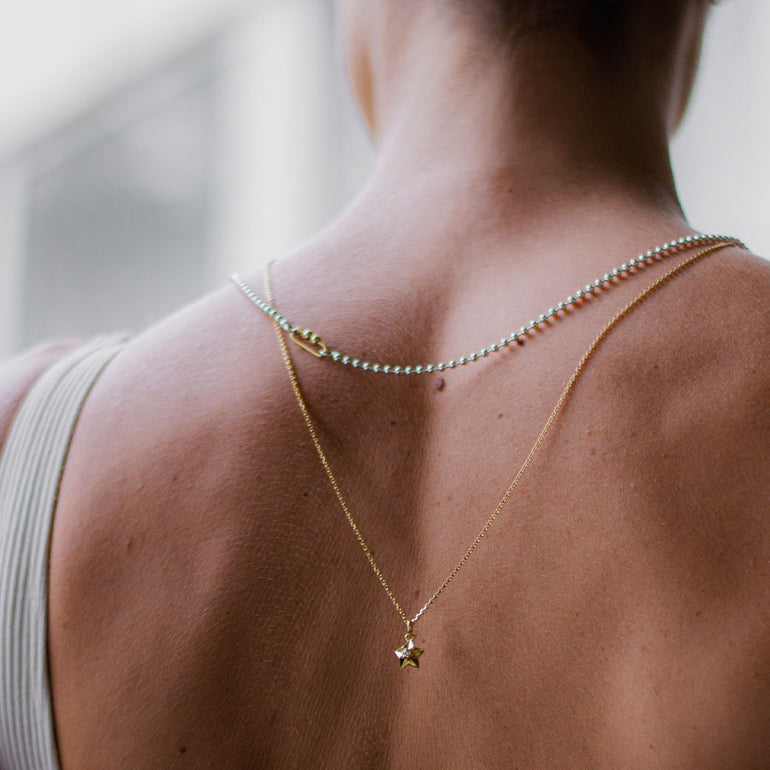Frau trägt silber Kugelkette und feine Goldkette mit mini Designer Stern Anhänger