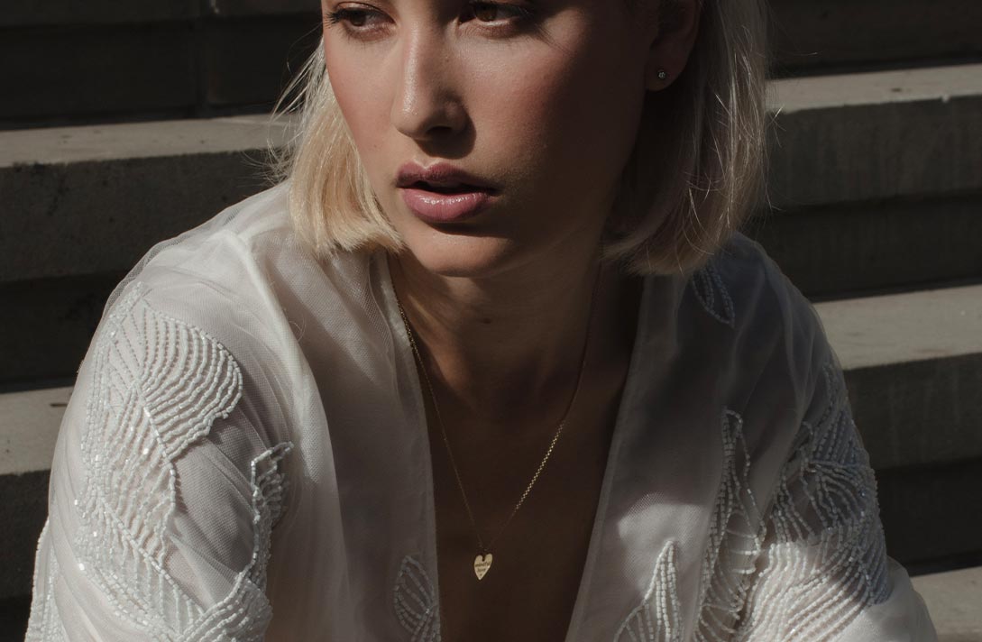 Model in weißem Kleid präsentiert den Talisman Herzanhänger an der Kette um ihren Hals aus recyceltem Gold von Maren Jewellery