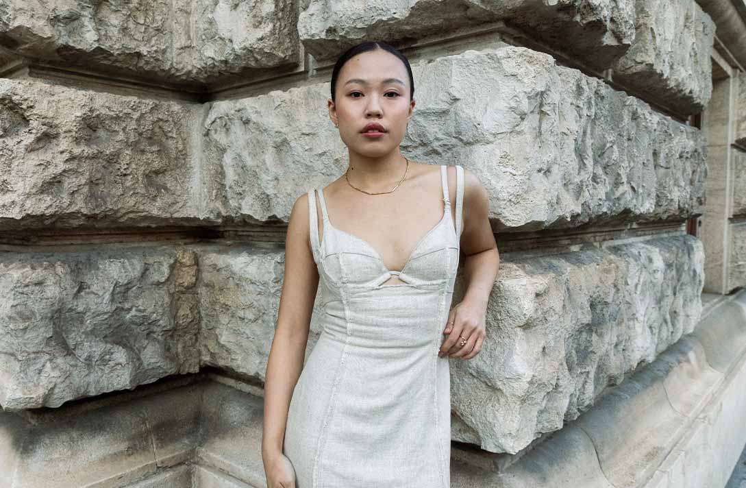 Asiatisches Model lehnt sich lässig gegen eine neoklassizistische Fasade und präsentiert nachhaltigen Schmuck von Maren Jewellery, einem transparent arbeitendem Schmucklabel