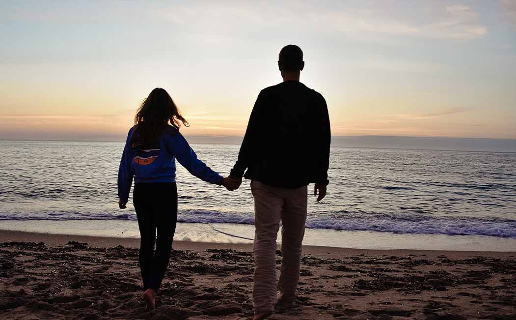 Engaged couple with a sustainable ring from Maren Jewellery standing at sunset on the beach holding hands
