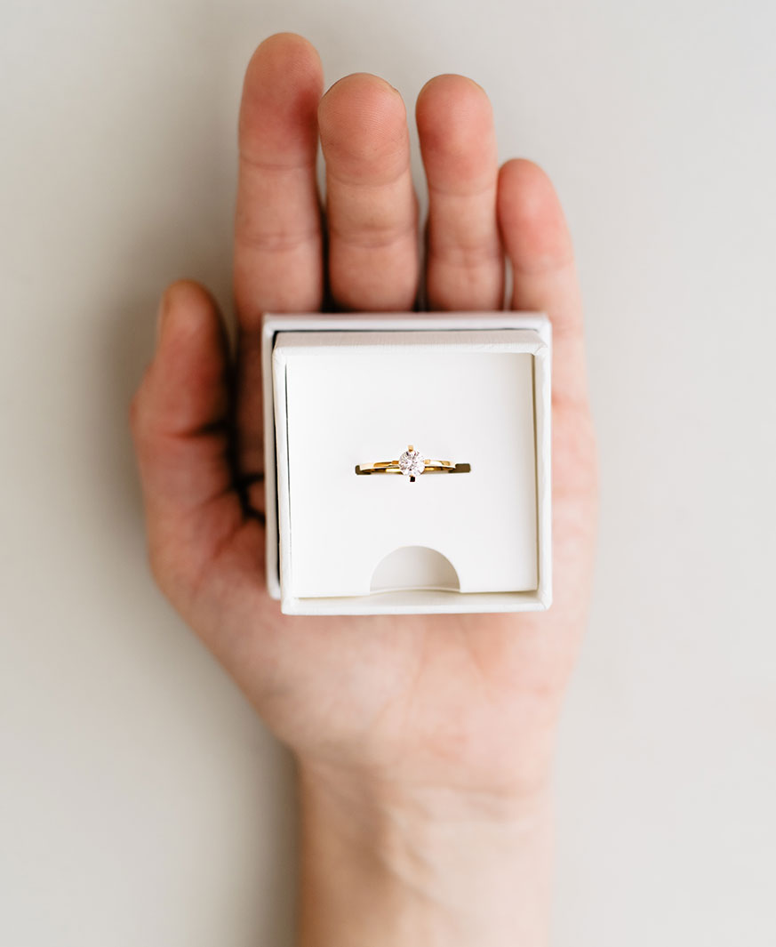 Eine Hand hält ein plastikfreies, hochwertiges Paper Case in dem ein handgemachter Verlobungsring aus recyceltem Gold mit Labordiamant steckt.