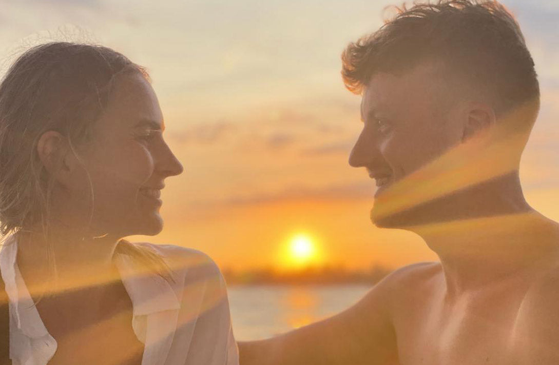 Frisch verlobtes Paar mit Verlobungsring von Maren Jewellery strahlt sich im Sonnenuntergang an
