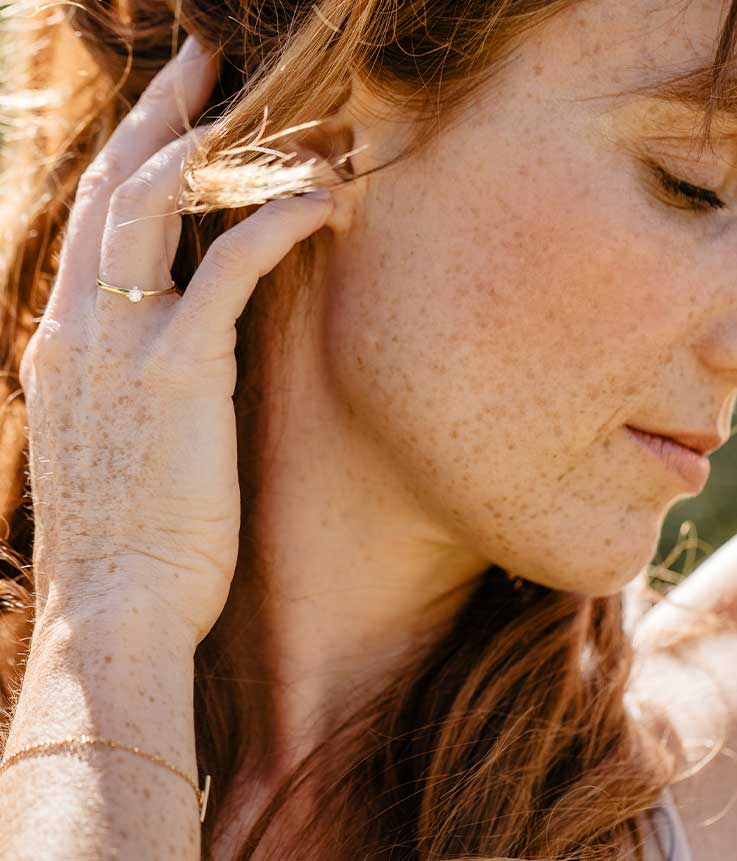 Potrait einer jungen Frau die sich zart durch ihre fährt mit nachhaltigem Goldschmuck an ihrer Hand