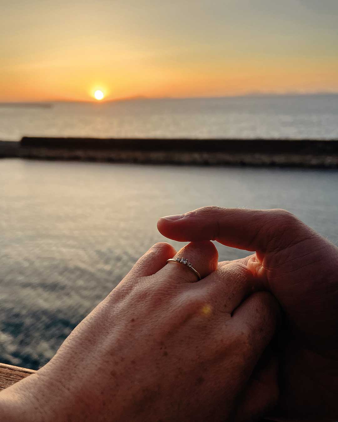 Freshly engaged couple with a sustainable, mindful engagement ring from Maren Jewellery by the sea at sunset