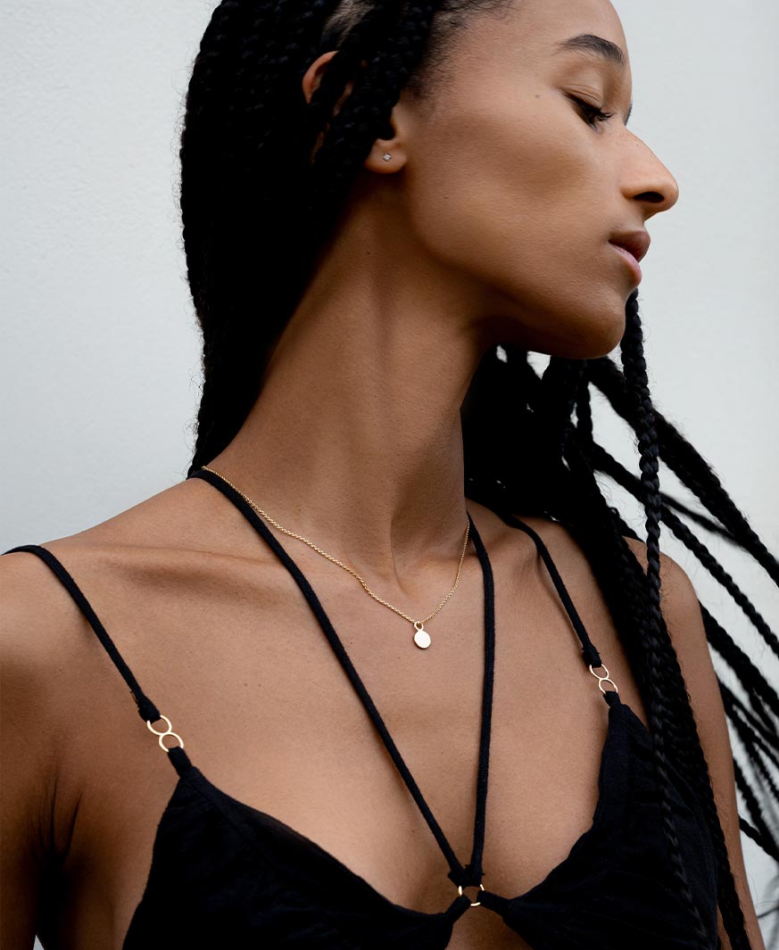 Münzanhänger mit Buchstabenprägung von Maren Jewellery aus recyceltem Gold an einer Halskette eines Models, das elegant zur Seite sieht